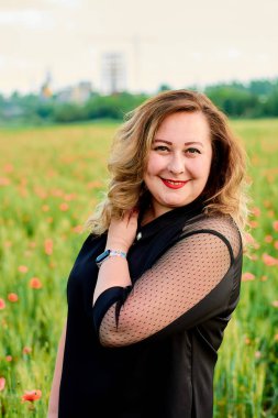 Artı yeşil buğday ve yabani haşhaş bir alanda siyah elbiseli bir kadın. Kilolu şişman kadın.