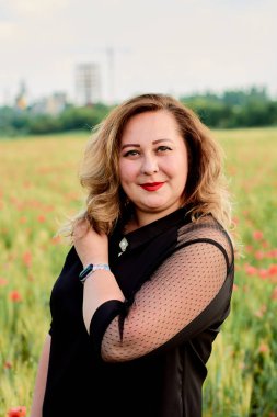 Artı yeşil buğday ve yabani haşhaş bir alanda siyah elbiseli bir kadın. Kilolu şişman kadın.