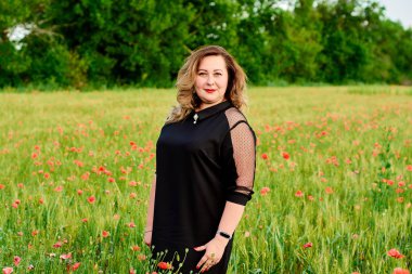 Artı yeşil buğday ve yabani haşhaş bir alanda siyah elbiseli bir kadın. Kilolu şişman kadın.