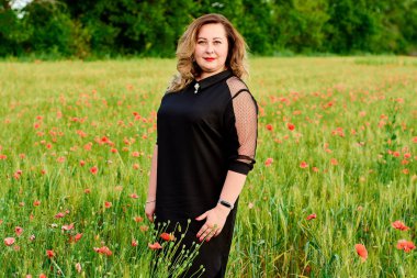 Artı yeşil buğday ve yabani haşhaş bir alanda siyah elbiseli bir kadın. Kilolu şişman kadın.