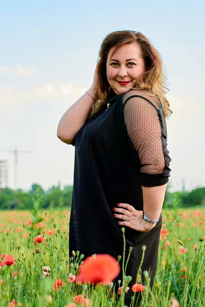 Plus Sized vrouw in een zwarte jurk op een gebied van groene tarwe en wilde papavers. Overgewicht dikke vrouw. — Stockfoto