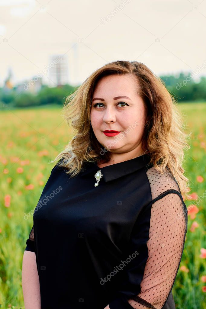 Plus sized woman in a black dress on a field of green wheat and wild poppies. Overweight fat woman.