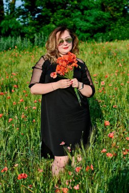 Artı yeşil buğday ve yabani haşhaş bir alanda siyah elbiseli bir kadın. Kilolu şişman kadın.