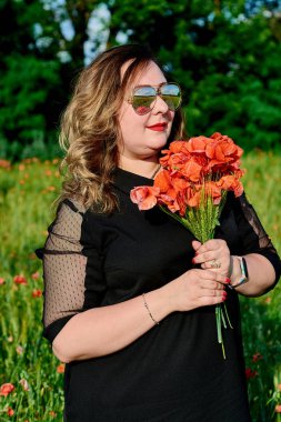 Artı yeşil buğday ve yabani haşhaş bir alanda siyah elbiseli bir kadın. Kilolu şişman kadın.