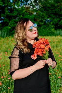 Artı yeşil buğday ve yabani haşhaş bir alanda siyah elbiseli bir kadın. Kilolu şişman kadın.