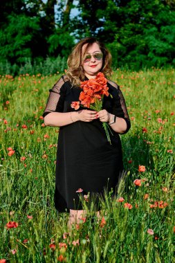 Artı yeşil buğday ve yabani haşhaş bir alanda siyah elbiseli bir kadın. Kilolu şişman kadın.