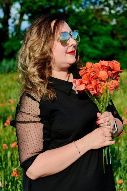 Artı yeşil buğday ve yabani haşhaş bir alanda siyah elbiseli bir kadın. Kilolu şişman kadın.