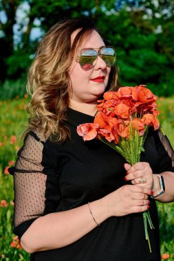 Artı yeşil buğday ve yabani haşhaş bir alanda siyah elbiseli bir kadın. Kilolu şişman kadın.