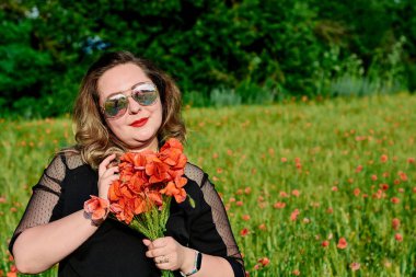 Artı yeşil buğday ve yabani haşhaş bir alanda siyah elbiseli bir kadın. Kilolu şişman kadın.