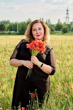 Artı yeşil buğday ve yabani haşhaş bir alanda siyah elbiseli bir kadın. Kilolu şişman kadın.