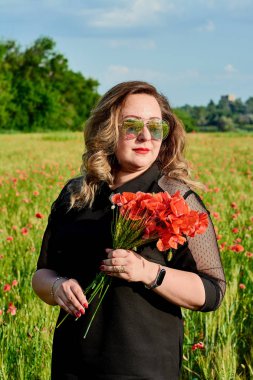 Artı yeşil buğday ve yabani haşhaş bir alanda siyah elbiseli bir kadın. Kilolu şişman kadın.