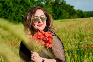 Artı yeşil buğday ve yabani haşhaş bir alanda siyah elbiseli bir kadın. Kilolu şişman kadın.