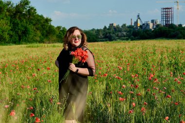 Artı yeşil buğday ve yabani haşhaş bir alanda siyah elbiseli bir kadın. Kilolu şişman kadın.