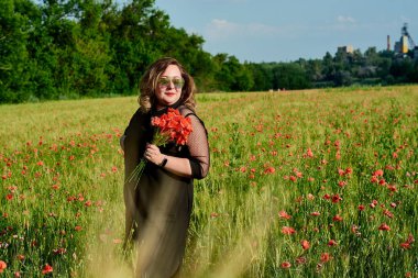 Artı yeşil buğday ve yabani haşhaş bir alanda siyah elbiseli bir kadın. Kilolu şişman kadın.