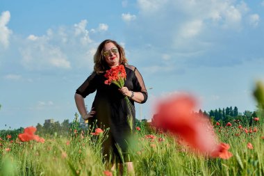 Artı yeşil buğday ve yabani haşhaş bir alanda siyah elbiseli bir kadın. Kilolu şişman kadın.