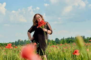 Artı yeşil buğday ve yabani haşhaş bir alanda siyah elbiseli bir kadın. Kilolu şişman kadın.