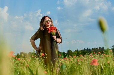 Artı yeşil buğday ve yabani haşhaş bir alanda siyah elbiseli bir kadın. Kilolu şişman kadın.