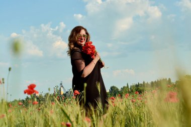 Artı yeşil buğday ve yabani haşhaş bir alanda siyah elbiseli bir kadın. Kilolu şişman kadın.