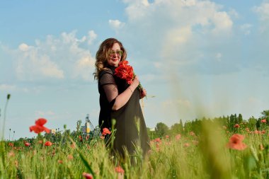 Artı yeşil buğday ve yabani haşhaş bir alanda siyah elbiseli bir kadın. Kilolu şişman kadın.