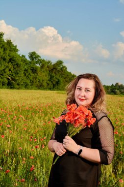 Artı yeşil buğday ve yabani haşhaş bir alanda siyah elbiseli bir kadın. Kilolu şişman kadın.
