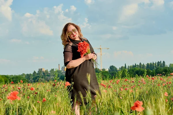 Плюс женщина в черном платье на поле из зеленой пшеницы и диких маков. Толстая толстая женщина . — стоковое фото