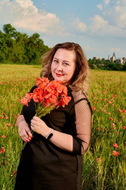 Artı yeşil buğday ve yabani haşhaş bir alanda siyah elbiseli bir kadın. Kilolu şişman kadın.