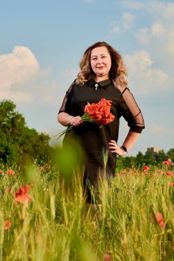 Artı yeşil buğday ve yabani haşhaş bir alanda siyah elbiseli bir kadın. Kilolu şişman kadın.