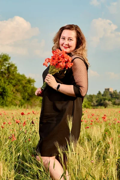 Além disso mulher de tamanho em um vestido preto em um campo de trigo verde e papoilas selvagens. Mulher gorda com excesso de peso . — Fotografia de Stock