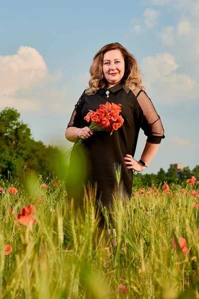 Συν το μέγεθος της γυναίκας με ένα μαύρο φόρεμα σε ένα χωράφι με πράσινο σιτάρι και άγριες παπαρούνες. Υπέρβαρη χοντρή γυναίκα. — Φωτογραφία Αρχείου