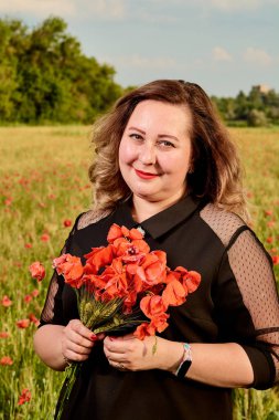 Artı yeşil buğday ve yabani haşhaş bir alanda siyah elbiseli bir kadın. Kilolu şişman kadın.