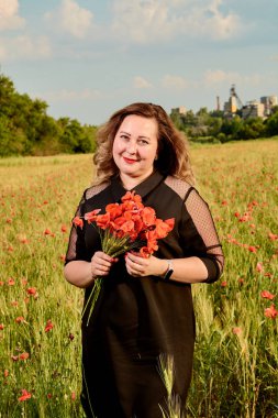 Artı yeşil buğday ve yabani haşhaş bir alanda siyah elbiseli bir kadın. Kilolu şişman kadın.