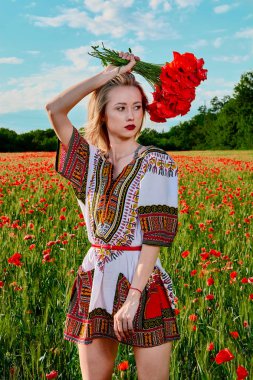 Yeşil buğday ve yabani haşhaş bir alanda beyaz kısa elbiseli uzun saçlı sarışın genç kadın.