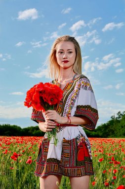 Yeşil buğday ve yabani haşhaş bir alanda beyaz kısa elbiseli uzun saçlı sarışın genç kadın.