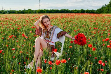 Yeşil buğday ve yabani haşhaş bir alanda beyaz kısa elbiseli uzun saçlı sarışın genç kadın.