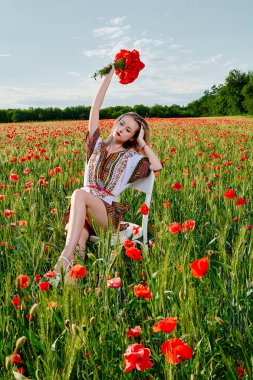 Yeşil buğday ve yabani haşhaş bir alanda beyaz kısa elbiseli uzun saçlı sarışın genç kadın.