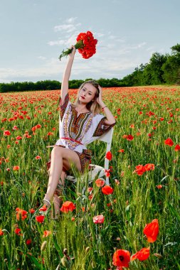 Yeşil buğday ve yabani haşhaş bir alanda beyaz kısa elbiseli uzun saçlı sarışın genç kadın.