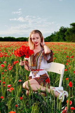 Yeşil buğday ve yabani haşhaş bir alanda beyaz kısa elbiseli uzun saçlı sarışın genç kadın.