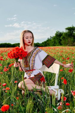 Yeşil buğday ve yabani haşhaş bir alanda beyaz kısa elbiseli uzun saçlı sarışın genç kadın.