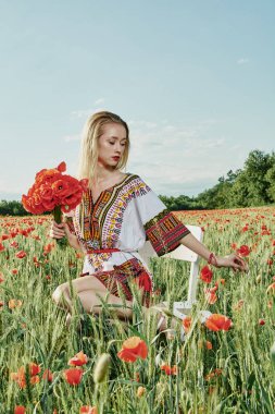 Yeşil buğday ve yabani haşhaş bir alanda beyaz kısa elbiseli uzun saçlı sarışın genç kadın.