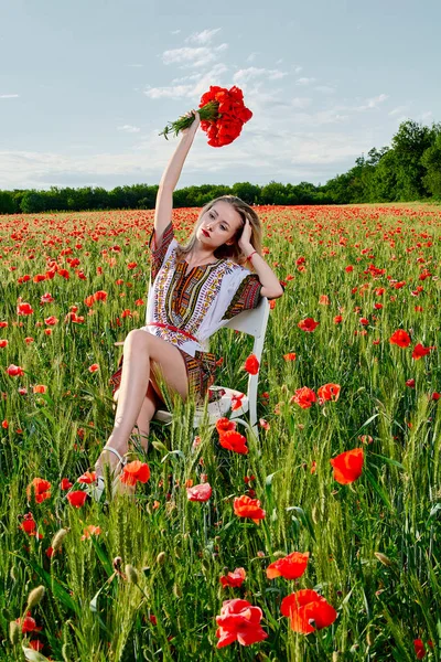 Yeşil buğday ve yabani haşhaş bir alanda beyaz kısa elbiseli uzun saçlı sarışın genç kadın.