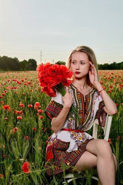 Yeşil buğday ve yabani haşhaş bir alanda beyaz kısa elbiseli uzun saçlı sarışın genç kadın.