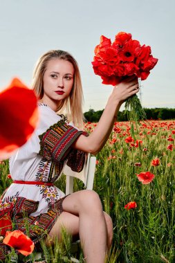 Yeşil buğday ve yabani haşhaş bir alanda beyaz kısa elbiseli uzun saçlı sarışın genç kadın.