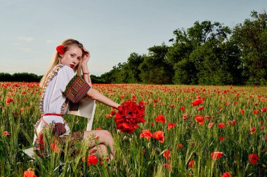Yeşil buğday ve yabani haşhaş bir alanda beyaz kısa elbiseli uzun saçlı sarışın genç kadın.