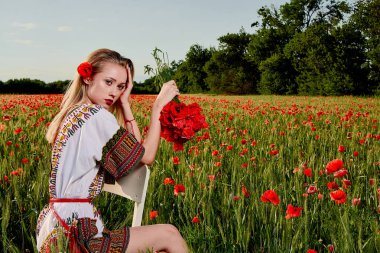 Yeşil buğday ve yabani haşhaş bir alanda beyaz kısa elbiseli uzun saçlı sarışın genç kadın.