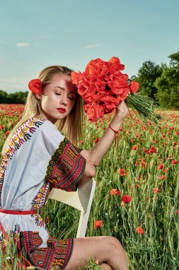 Yeşil buğday ve yabani haşhaş bir alanda beyaz kısa elbiseli uzun saçlı sarışın genç kadın.