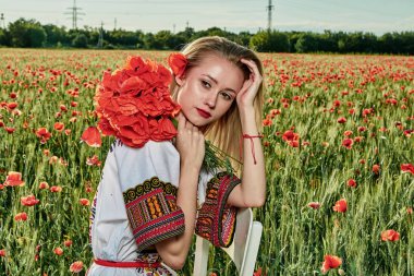 Yeşil buğday ve yabani haşhaş bir alanda beyaz kısa elbiseli uzun saçlı sarışın genç kadın.