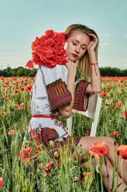 Yeşil buğday ve yabani haşhaş bir alanda beyaz kısa elbiseli uzun saçlı sarışın genç kadın.