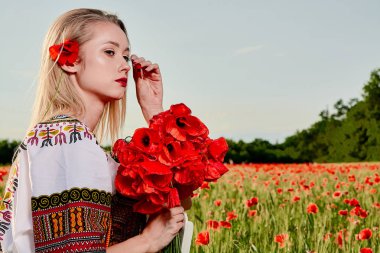 Yeşil buğday ve yabani haşhaş bir alanda beyaz kısa elbiseli uzun saçlı sarışın genç kadın.