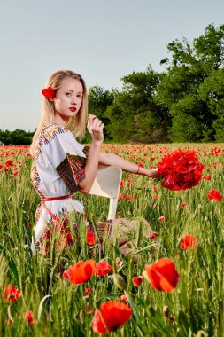 Yeşil buğday ve yabani haşhaş bir alanda beyaz kısa elbiseli uzun saçlı sarışın genç kadın.