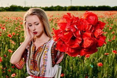 Yeşil buğday ve yabani haşhaş bir alanda beyaz kısa elbiseli uzun saçlı sarışın genç kadın.